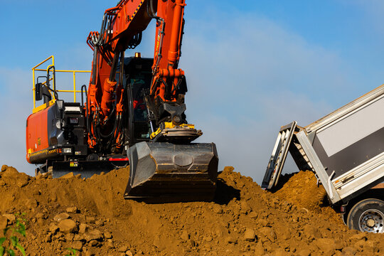 Excavator earthmoving equipment working at construction site beside truck dumping dirt