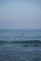 Calm sea at dawn with soft pastel blue and pink tones. Gentle waves approaching the shore under a peaceful, minimalistic horizon.