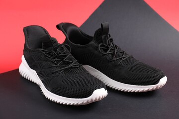 Pair of black sneakers on color background, closeup