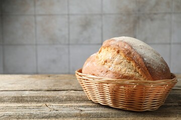 Loaf of fresh bread in wicker basket on wooden table, closeup. Space for text
