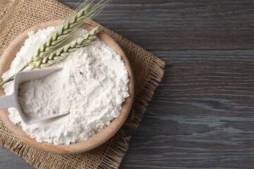 Flour in bowl and green wheat spikes on wooden table, top view. Space for text