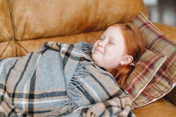 Young girl enjoying a cozy moment wrapped in a blanket while resting on a sofa