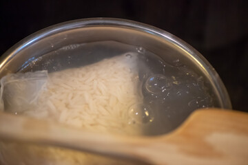 A candid kitchen scene showing a woman preparing rice, as boiling water steams from the pot