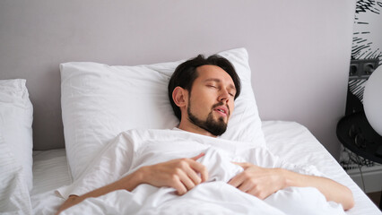 Portrait of a young brunette man sleeping soundly in a soft, cozy bed bathed in early morning light
