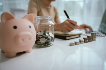 An Asian woman is writing in a notebook and stacking coins and a piggy bank, which symbolizes...
