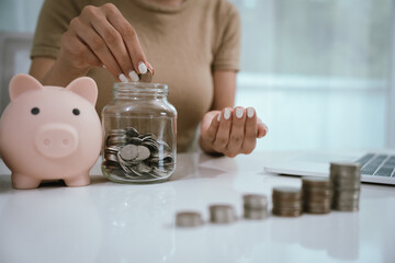 An Asian woman is writing in a notebook and stacking coins and a piggy bank, which symbolizes...
