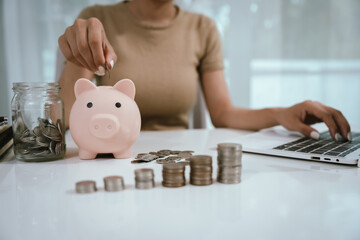 An Asian woman is writing in a notebook and stacking coins and a piggy bank, which symbolizes...