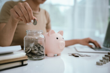 An Asian woman is writing in a notebook and stacking coins and a piggy bank, which symbolizes...