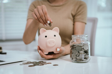 An Asian woman is writing in a notebook and stacking coins and a piggy bank, which symbolizes...