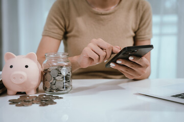 An Asian woman is writing in a notebook and stacking coins and a piggy bank, which symbolizes...