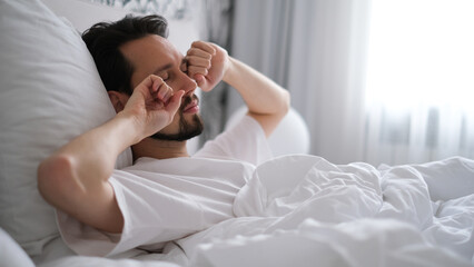 Young brunette man yawning and stretching after waking up in the morning