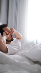 Young brunette man yawning and stretching after waking up in the morning