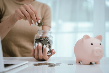 An Asian woman is writing in a notebook and stacking coins and a piggy bank, which symbolizes...