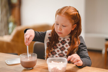 Child engages in fun kitchen activity mixing chocolate dessert with marshmallows at home in cozy living room during afternoon