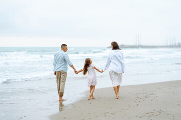 Happy young family walking together on the beach holding hands. Man with his pregnant wife and daughter enjoying time together feeling freedom outdoors. Family, weekend concept.