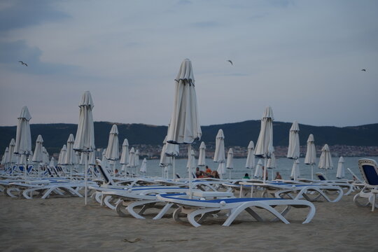 closed beach umbrellas and empty sun loungers on the coast of Golden Sands resort in Bulgaria, early morning or off-season, overcast sky and calm sea, tranquil beach scene - Powered by Adobe