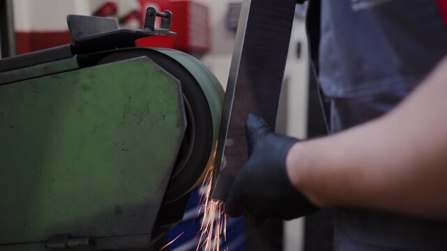Close-up of a worker sharpening a metal bar on an industrial belt grinder, with visible sparks flying during the grinding process. Concept of precision, craftsmanship, and metal fabrication.