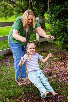 Mother pushing Six year old child on swing in country hanging from jacaranda tree