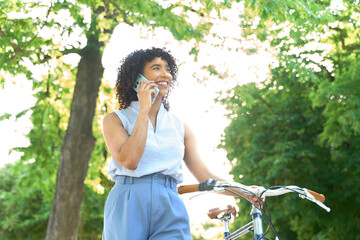 Young manager walking with bicycle and talking on smartphone in a park