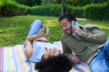 Happy couple lying on blanket using smartphones in park