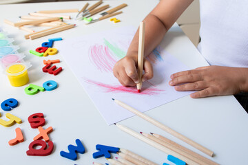 Child drawing with colored pencils and alphabet letters on white table