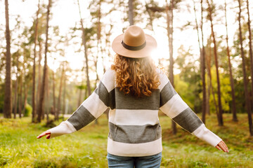 Portrait of a cheerful woman in a hat in the sunbeams on a clearing in a dense forest. Beautiful woman enjoying a walk in the park. Weekend and enjoyment concept. Active lifestyle. © maxbelchenko