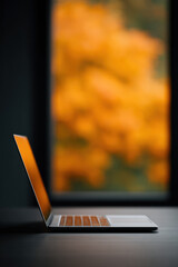 Sleek laptop sits on table with vibrant orange autumn background, creating warm and focused atmosphere