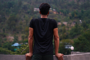Man seen from behind, leaning on a wall, admiring mountainous landscape. Ideal for travel,...