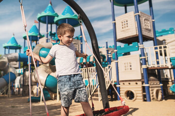 Preschool boy swinging on swings against the background of a large children's town in the shape of...