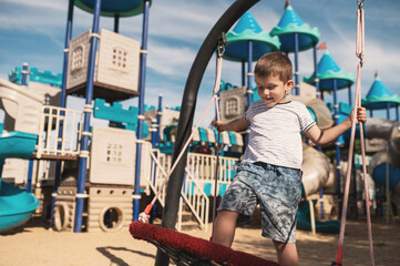 Preschool boy swinging on swings against the background of a large children's town in the shape of...