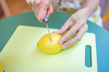 A close-up view of hands using a knife to prepare a lemon on a cutting board, showcasing culinary skills and fresh ingredients