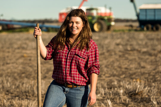 Smiling female farmer standing in agricultural field with rake