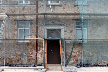 Old brick building under renovation with scaffolding mesh and construction fence