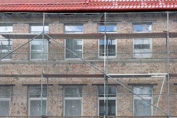 Old brick building facade under restoration with scaffolding mesh and metal framework.