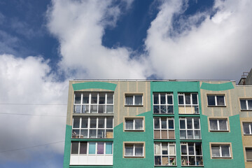 Colorful facade of residential apartment building with balconies and windows under blue sky with clouds.