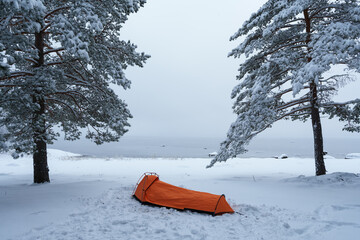 Orange tent in a winter forest on the lake shore.