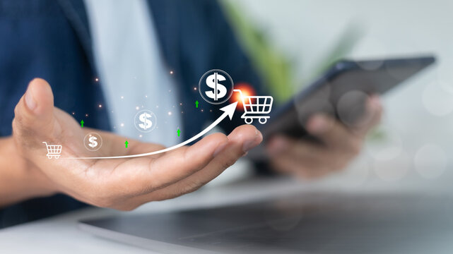 Hand holding digital graph with dollar signs and shopping cart icon, symbolizing growth in online sales, ecommerce revenue, and business profit strategy. - Powered by Adobe
