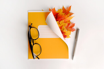 Layout of a yellow school diary or notebook with bright maple leaves, glasses, and a pen on a white background. Teacher's Day concept, students. 1st of September card. Back to school. Copyspace