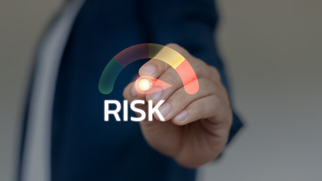Hand pointing at colorful risk level meter gauge, concept of business risk, financial analysis, cybersecurity warning, and strategic decision making.