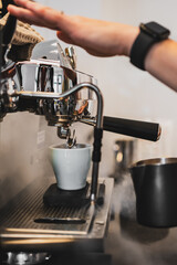 Barista's hand brewing espresso in a white cup with rising steam, showcasing professional coffee preparation in a café setting