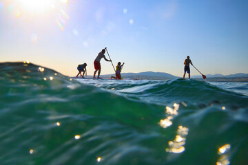 family with kids  riding  on sup surfing in the sea at summer day.