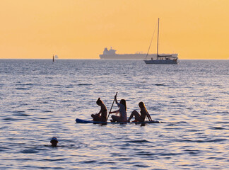 young girls  riding  on sup surfing in the sea at sunset.