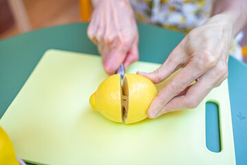 A woman carefully slices a lemon in half on a bright yellow cutting board, preparing it for use in cooking or baking