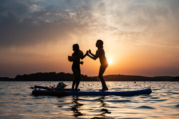 Two girls playing on paddle board at sunset