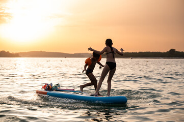 Children balancing on paddle board at sunset during summer vacation