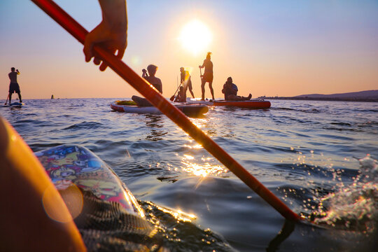 young people  riding  on sup surfing in the sea at sunset.