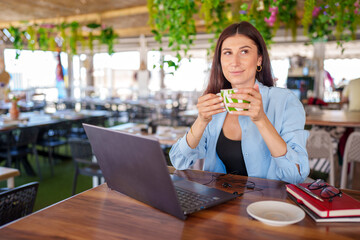 Professional woman sipping cappuccino, working on laptop at contemporary cafe, blending productivity with leisure moment