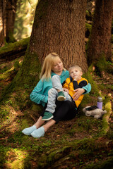 A young grandmother and her grandson are sitting under a tree hugging and drinking tea under a tree...