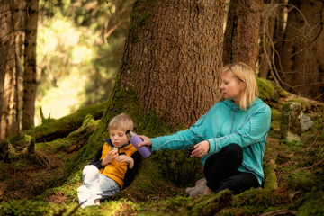 Young grandmother and her grandson drinking tea together under a tree in the forest. Warm family moment, eco lifestyle, bonding in nature. Peaceful outdoor break during a walk in the woods.