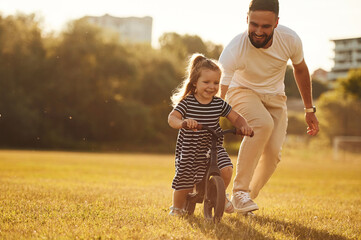Riding the bicycle. Father with his little daughter are on the field